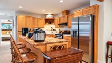 A modern kitchen with wooden cabinets, a stainless steel refrigerator, a large island with bar stools, and a built-in oven.