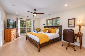 A bedroom with a bed, a desk, a chair, a television, and a ceiling fan.