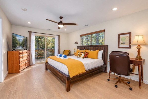 A bedroom with a bed, a desk, a chair, a television, and a ceiling fan.