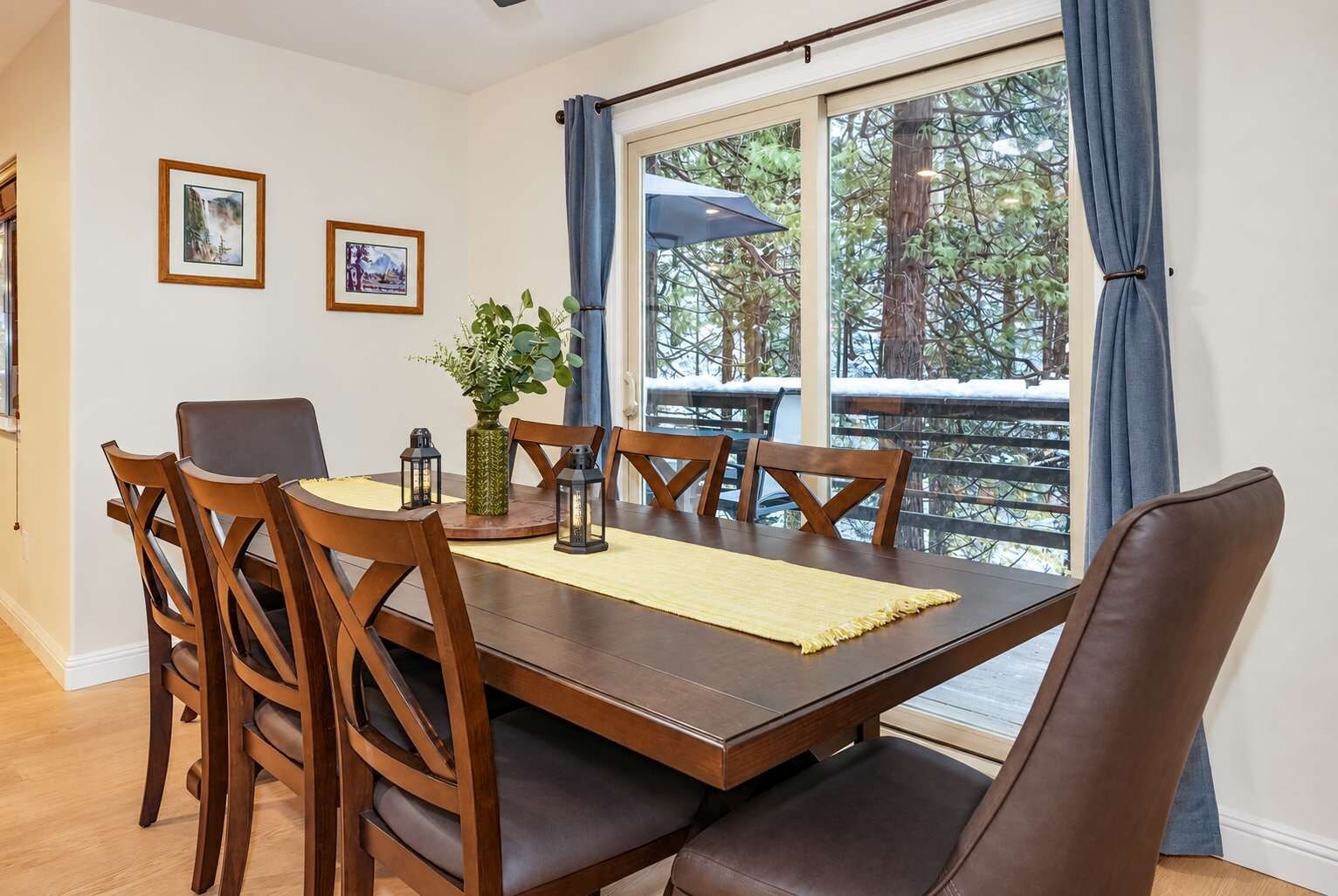 A dining area with a wooden table, chairs, and a view of a snowy deck through large windows.