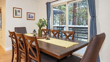 A dining area with a wooden table, chairs, and a view of a snowy deck through large windows.