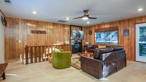 A cabin interior with wooden walls, a fireplace, a television, and a large window with a snowy view.
