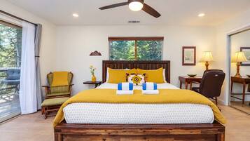 A bedroom with a bed, a desk, a chair, a ceiling fan, and a window with a view of trees.