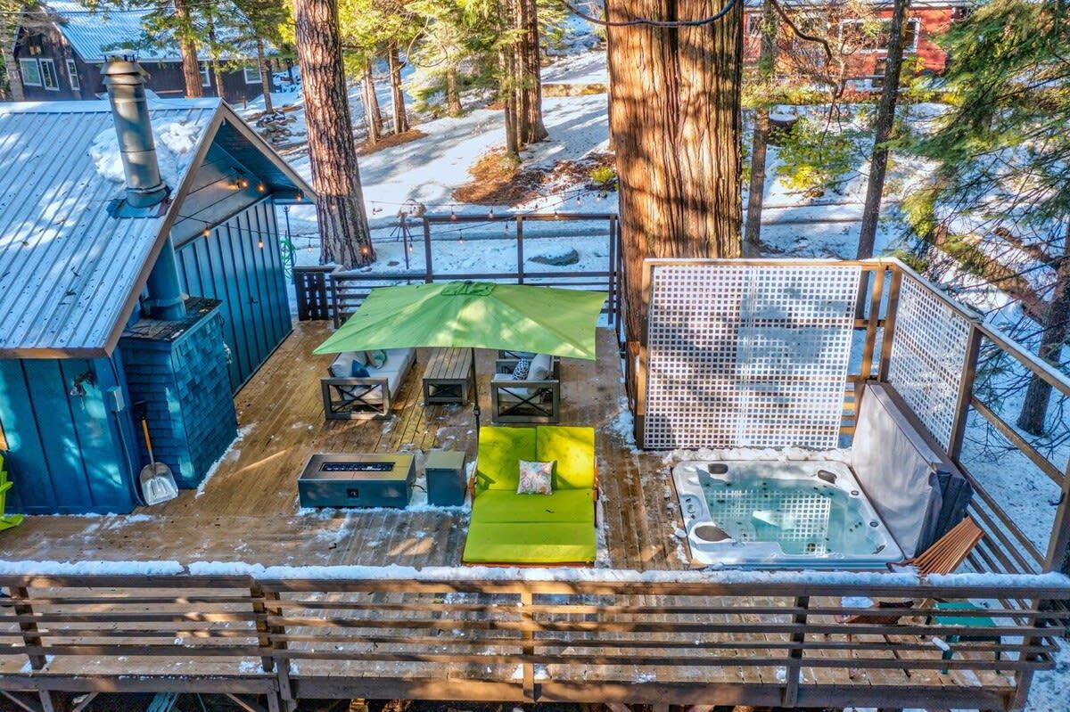 A wooden deck with a hot tub, a green umbrella, and a seating area with cushions.