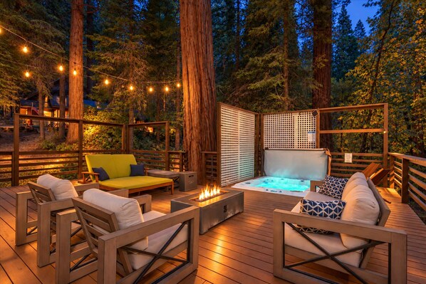 Een terras buiten met houten meubilair, een jacuzzi en lichtslingers.
