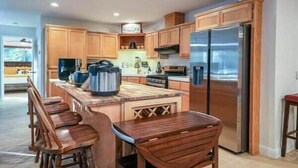 A modern kitchen with wooden cabinets, a central island with bar stools, a stainless steel refrigerator, and a built-in oven.