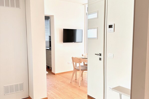 A modern hotel room with a wooden floor, a dining area with a table and chairs, a flat-screen TV mounted on the wall, and a white wardrobe with a mirror. - Villa Ada at the Lido (Venezia)