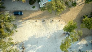 Vue aérienne d’un parking où se trouve une voiture, entourée d’arbres et d’un bâtiment dont le toit est bleu.