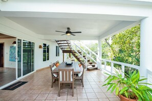 Eine überdachte Terrasse mit Esstisch und Stühlen, einem Deckenventilator und einer Treppe zu einer oberen Ebene.