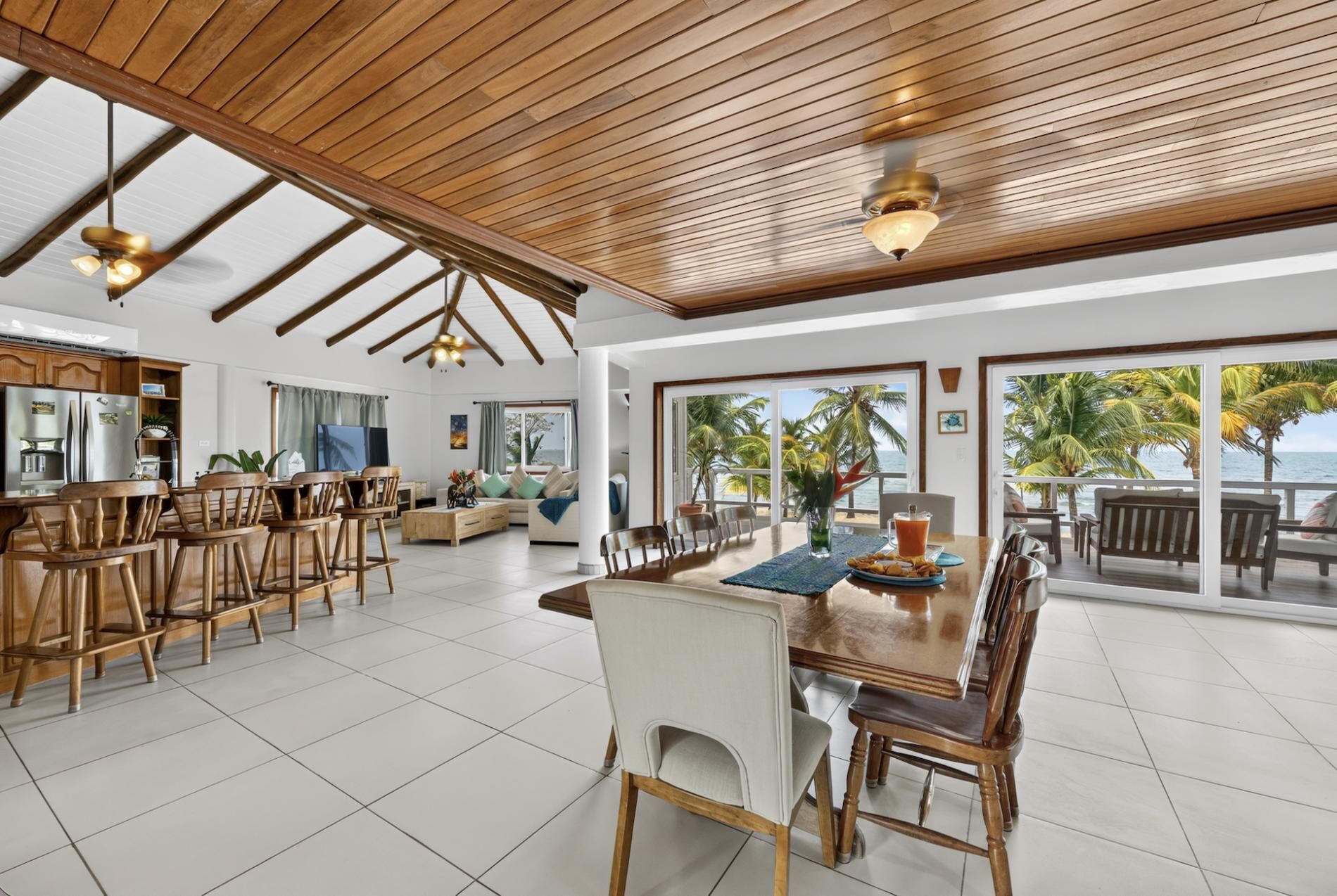 A spacious living area with a wooden ceiling, a kitchen with stainless steel appliances, and a dining area with a view of the ocean.