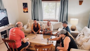 A group of people playing cards around a wooden coffee table in a living room with a television, a lamp, and a painting on the wall. - Private Oceanfront 4-Bed Villa w/Pool on Huge Lot (Placencia)