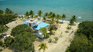 A beachfront property with a blue-roofed building, a thatched-roof structure, and a sandy beach with palm trees. - Private Oceanfront 4-Bed Villa w/Pool on Huge Lot (Placencia)