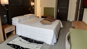 A hotel room with a bed, bedside tables, a nightstand, a wall-mounted lamp, a door, and a small wooden table. - Arsenale Turin Room 3 (Torino)