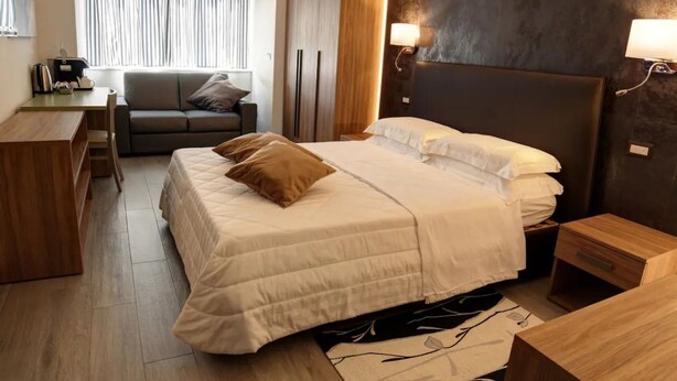 A modern hotel room with a bed, a desk, a sofa, and a large window with curtains. - Arsenale Turin Room 3 (Torino)