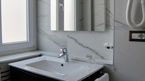 Un baño con un lavamanos blanco, un espejo y un perchero para toallas.