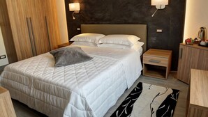 Una habitación de hotel moderna con una cama grande, mesitas de noche, un armario y lámparas fijadas a la pared.