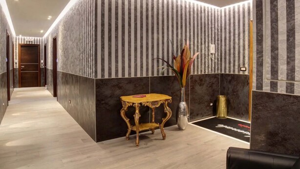 Un moderno vestíbulo de hotel con un mostrador de recepción de madera, un florero con plantas decorativas y una pared a rayas negras y blancas.