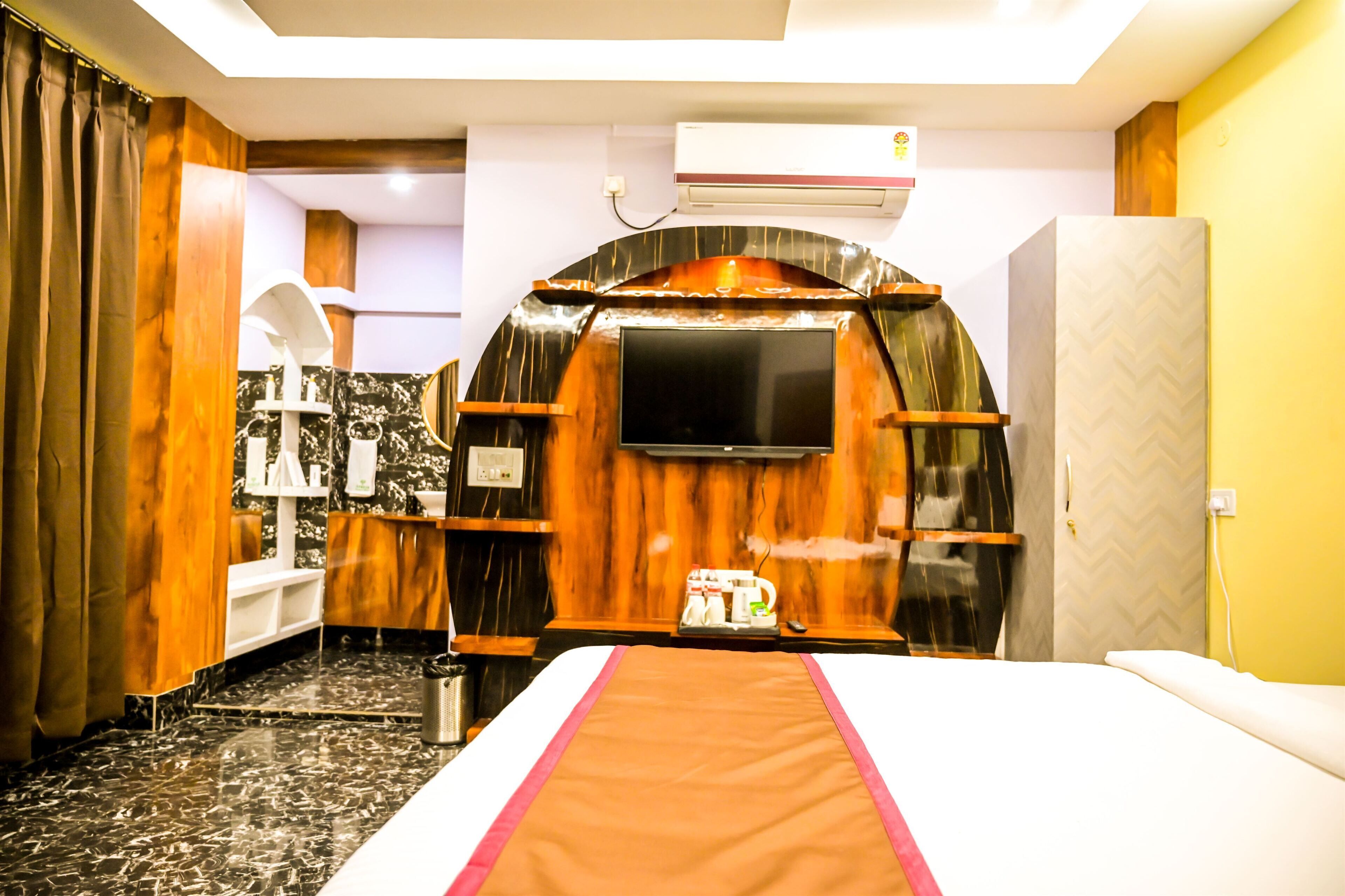 Habitación de hotel con cama, televisión montada en una pared de madera, baño con piso de mármol y un minibar.