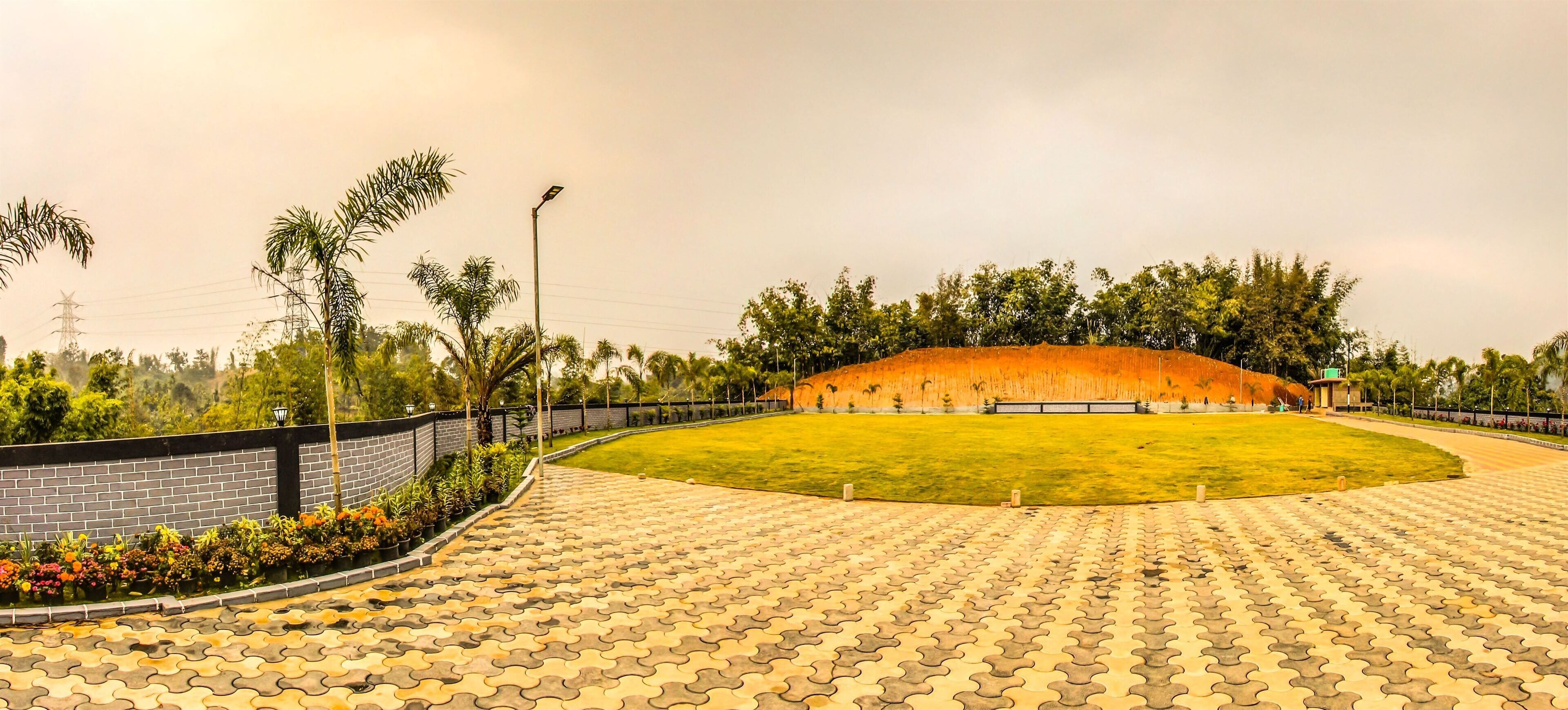 A paved outdoor area with a curved pathway, a grassy field, and a brick wall with a flower bed.