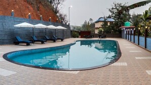 Uma piscina com espreguiçadeiras e guarda-sóis, cercada por um muro de pedra e um deck pavimentado.
