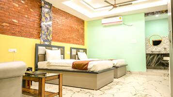 A hotel room with a bed, a small table, a chair, a ceiling fan, and a bathroom with a mirror and sink.