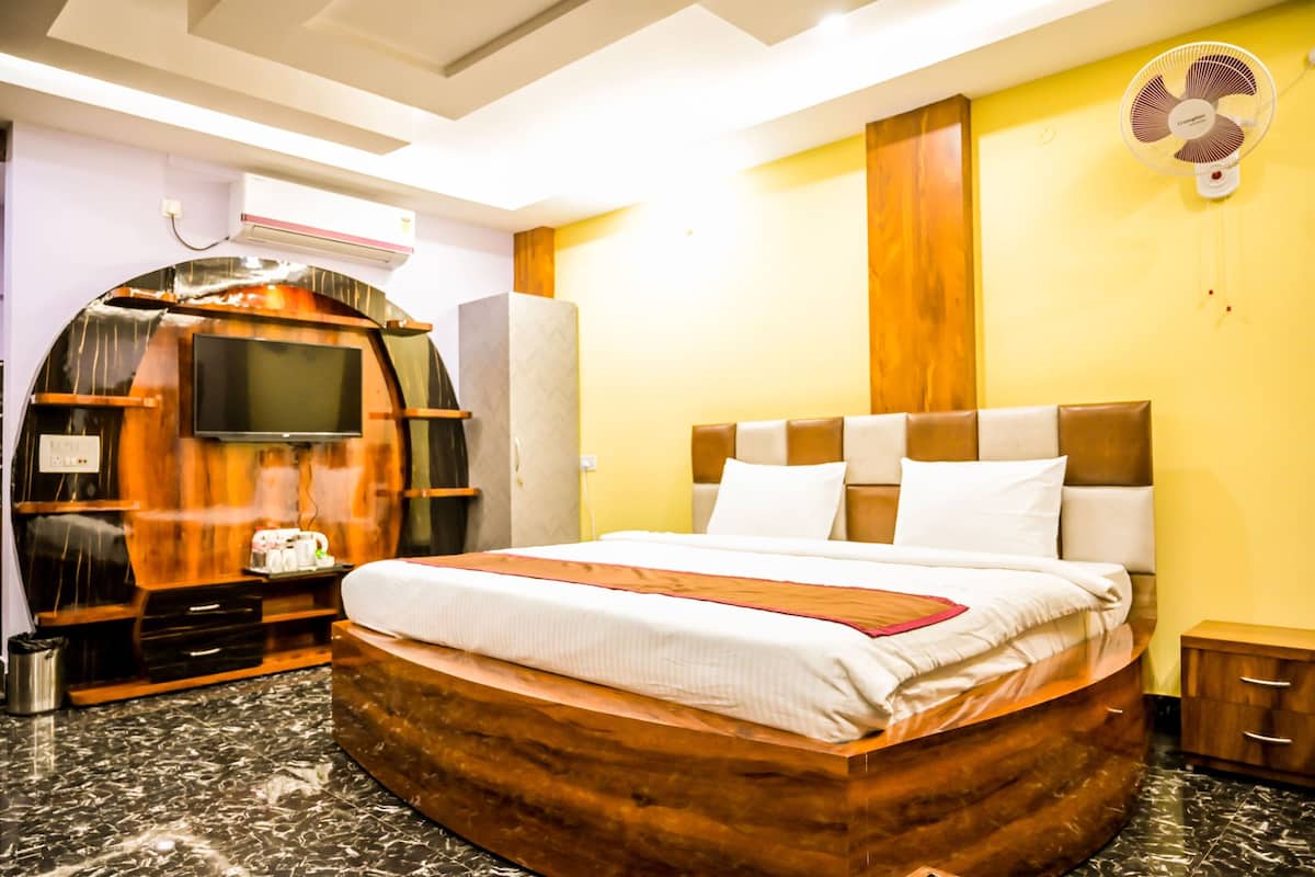 Une chambre d’hôtel avec un grand lit, un téléviseur fixé à un mur en bois, un ventilateur et un petit meuble.