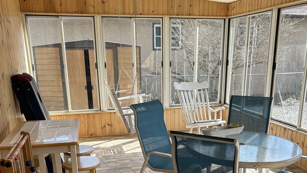 A sunlit room with a wooden ceiling, large windows, a ceiling fan, a table with chairs, and a wooden playset. - Spacious Home Away from Home (Columbus)