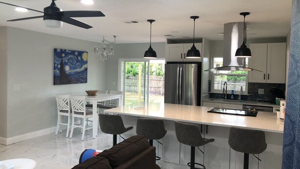 A modern kitchen with a central island, bar stools, and a dining area with white chairs. - Cozy ,Tranquil 3-bedroom in Spring Hill with WiFi, AC ; home away from home.  (Spring Hill)