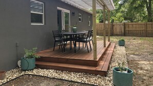 A patio with a table and chairs, a pergola, and a wooden deck. - Cozy ,Tranquil 3-bedroom in Spring Hill with WiFi, AC ; home away from home.  (Spring Hill)