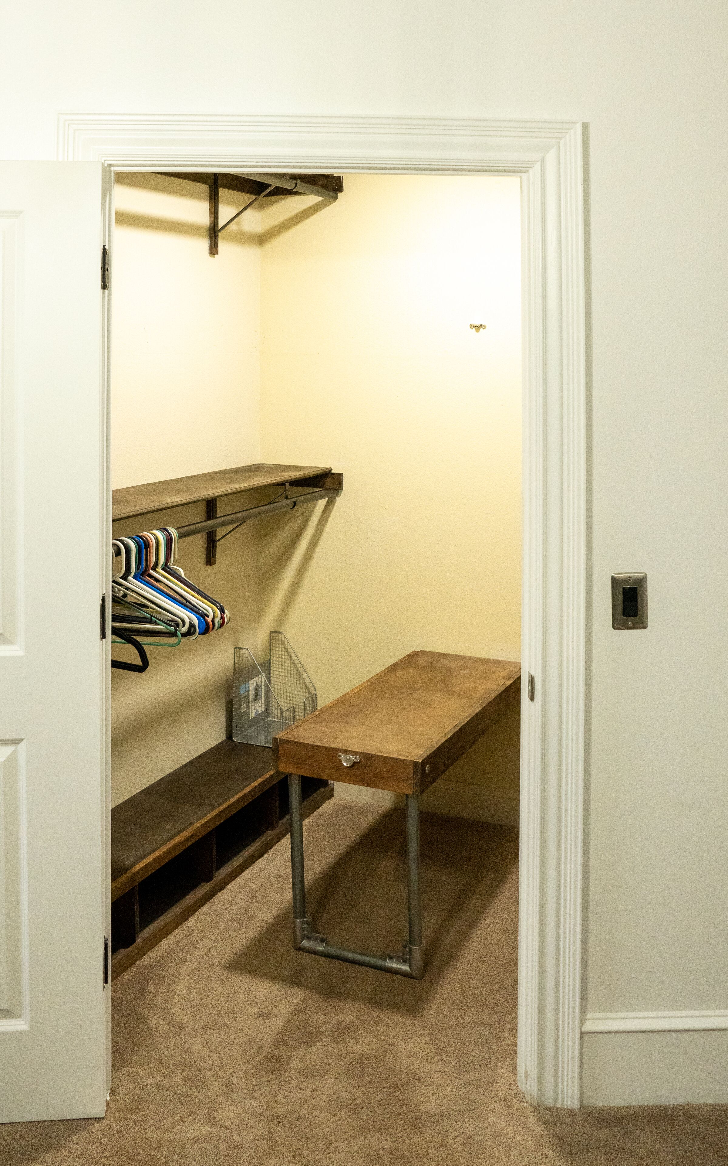 A room with a wooden bench, a metal table, and a clothing rack with hangers.