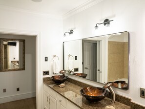 A bathroom with a large mirror, two vessel sinks, a towel rack, and a door leading to another room. - Located within the heart of the entertainment district! ADA ramp/parking on site (Fayetteville)