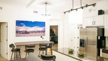 A modern kitchen with a stainless steel refrigerator, a bar area with stools, and a large painting of a mountain landscape on the wall.