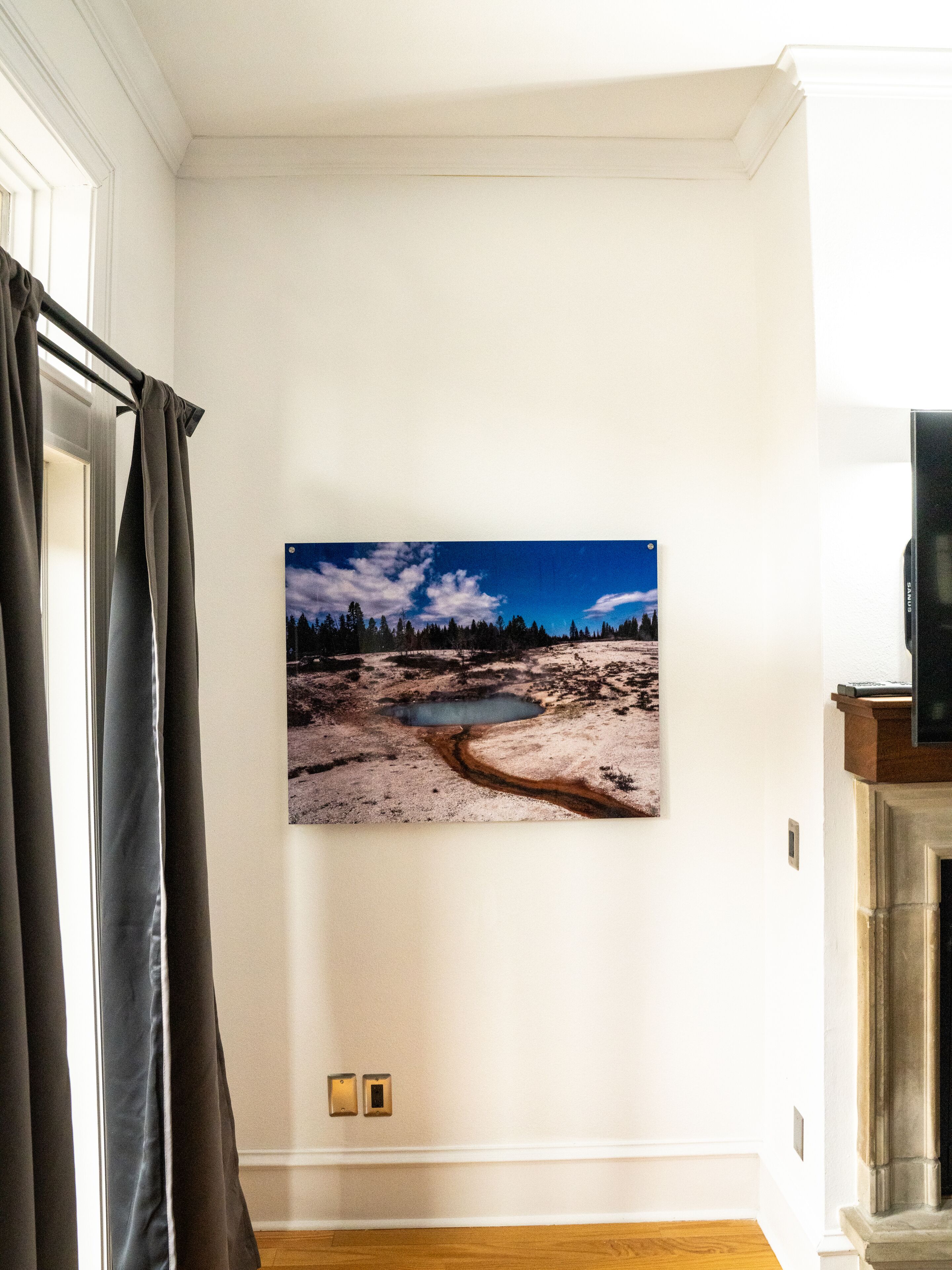 Una stanza con un grande quadro che raffigura un paesaggio, un pavimento in legno e una porta con tende.