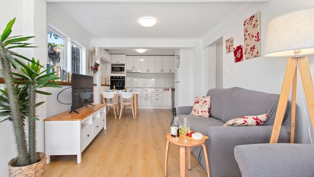 Un espacio habitable compacto con kitchenette, zona de comedor y sala de estar con sofá gris y una mesita.