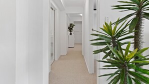 Un pasillo estrecho con paredes blancas y alfombra beige, que lleva a una habitación con una puerta al final.
