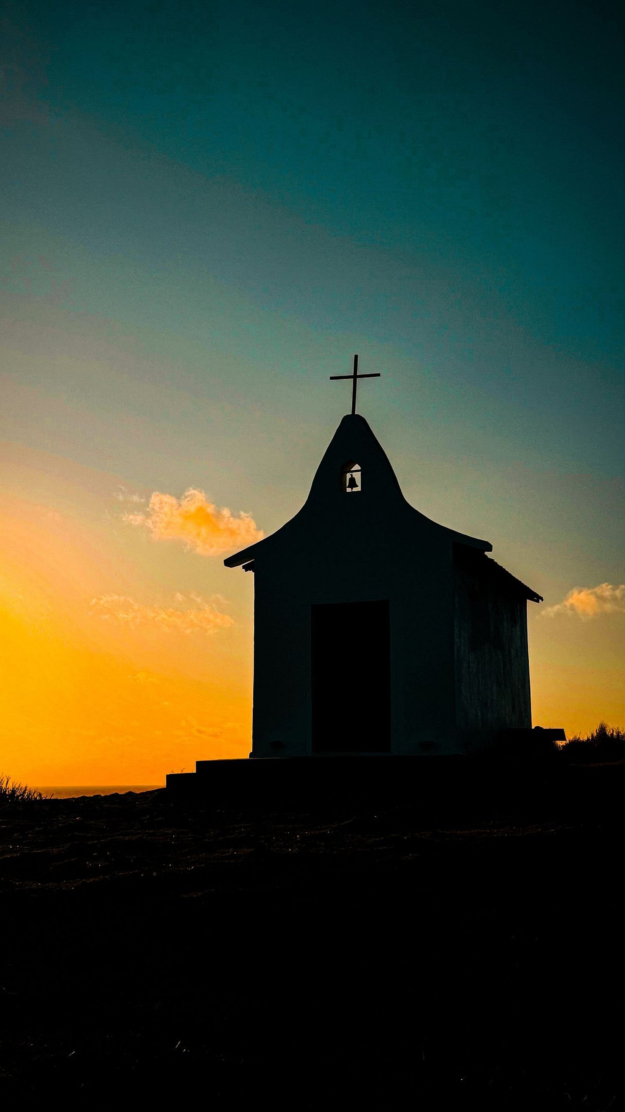 A small building with a cross on top, likely a church, with a clear sky in the background.
