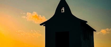 Un edificio pequeño con una cruz en la parte superior, probablemente una iglesia, con un cielo despejado al fondo.