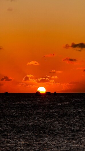 Ein Sonnenuntergang über einem Gewässer, mit einem Schiff und einer kleinen Struktur in der Ferne.