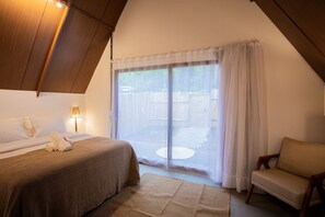 A bedroom with a bed, a chair, a lamp, and a view through a window with curtains.
