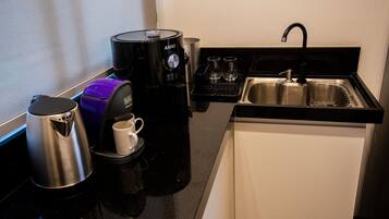 A compact kitchen with a coffee maker, a kettle, and a sink.