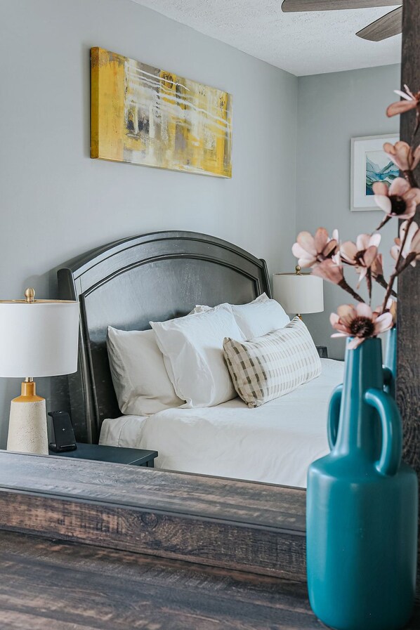 A bedroom with a bed, bedside lamps, a vase with flowers, and a painting on the wall.