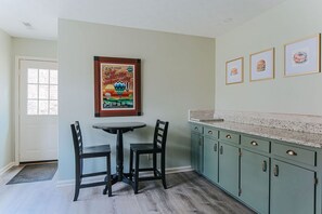 A kitchen with teal cabinets, a small dining table, and chairs. There is a framed poster on the wall and three framed pictures above the cabinets. - Tucked Inn: Upper Unit - 151 Getaway/Wine + Brews (Nellysford)
