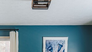 Ett rum med turkosa väggar, en inramad abstrakt målning, ett soffbord i trä, en soffa och en lampa.