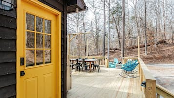 A wooden deck with a yellow door, a table with chairs, and a rocking chair.