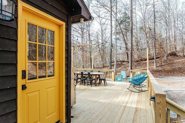 A wooden deck with a yellow door, a table with chairs, and a rocking chair.
