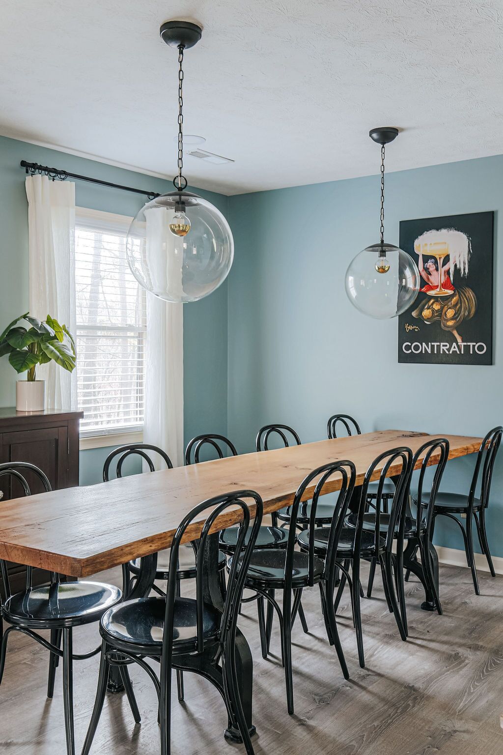 Un coin repas avec une table en bois et des chaises noires, un ventilateur de plafond et une affiche accrochée au mur.