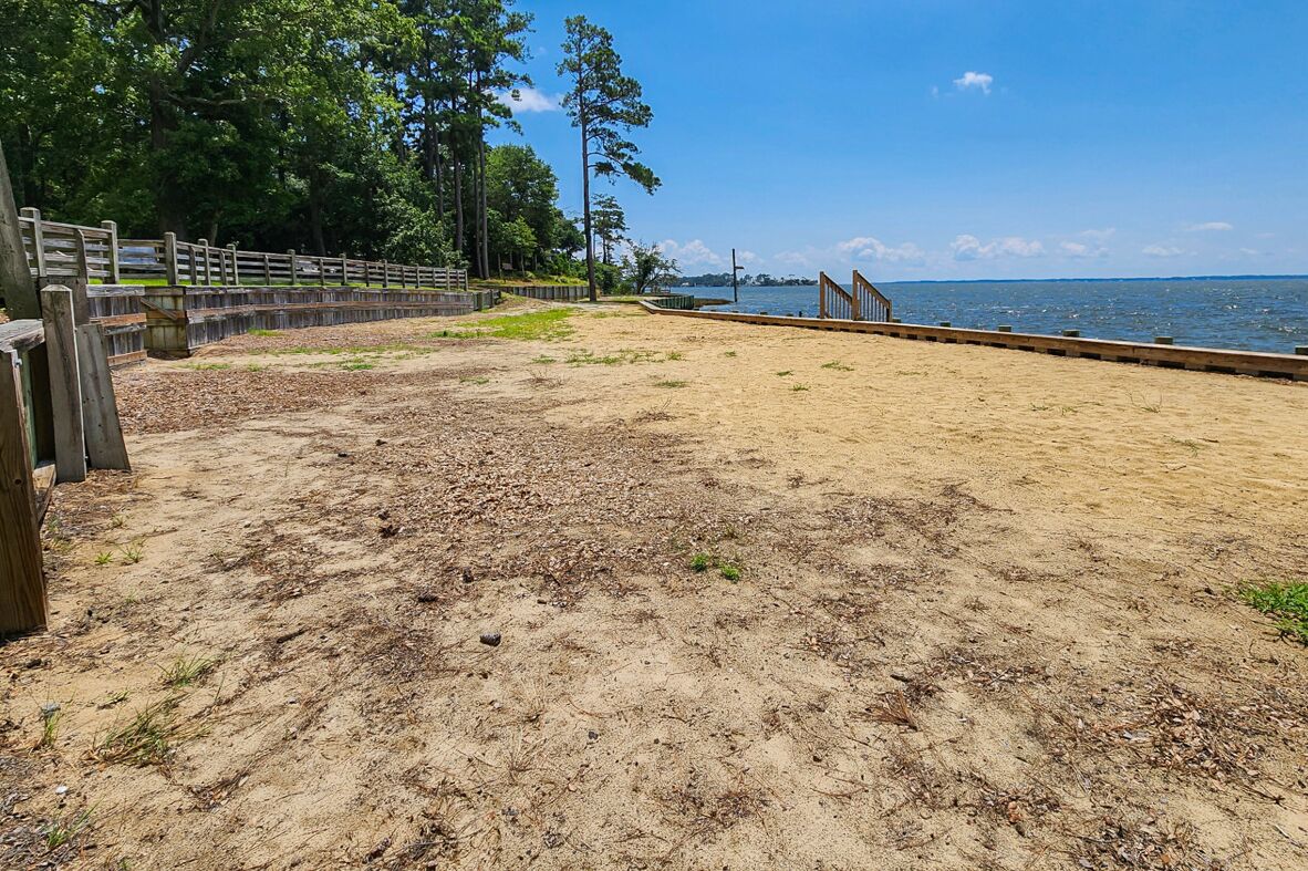 A sandy beach area with a wooden fence and a view of the water.