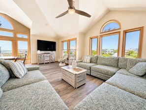A spacious living room with a large sectional sofa, a wooden coffee table, and a ceiling fan. - Osprey's Catch - Spacious Oceanside 8 BR Duck home w/pool, hot tub &  GOLF CART (Duck)