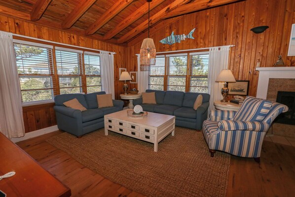 A cozy living room with wooden walls, a blue sofa, a striped armchair, and a fireplace.