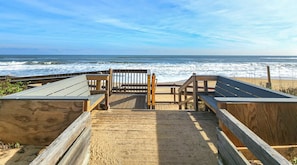 A wooden boardwalk leading to a beach with a wooden bench and a sign.